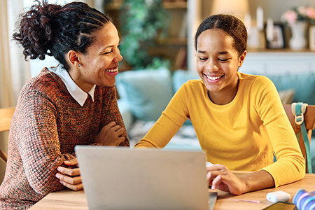 A student working on a laptop with her mother sitting next to her at the table