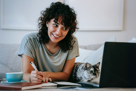 Student on laptop writing notes with a cat